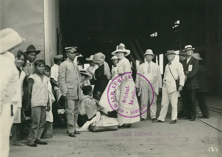 Tourist group after the arrival of a Hapag ocean-going passenger ship, local children and a local uniformed man at the entrance to the hall of Pier 5.