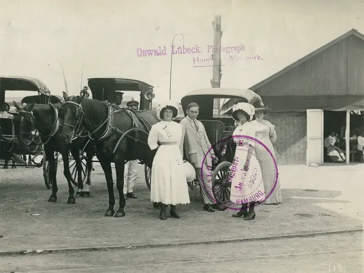 Tourists posing with a horse-drawn carriage and local driver in front of a hall after the arrival of a Hapag ocean-going passenger steamer.