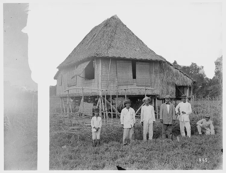 A boy, local men of different ages and a tourist in front of a simple hut.